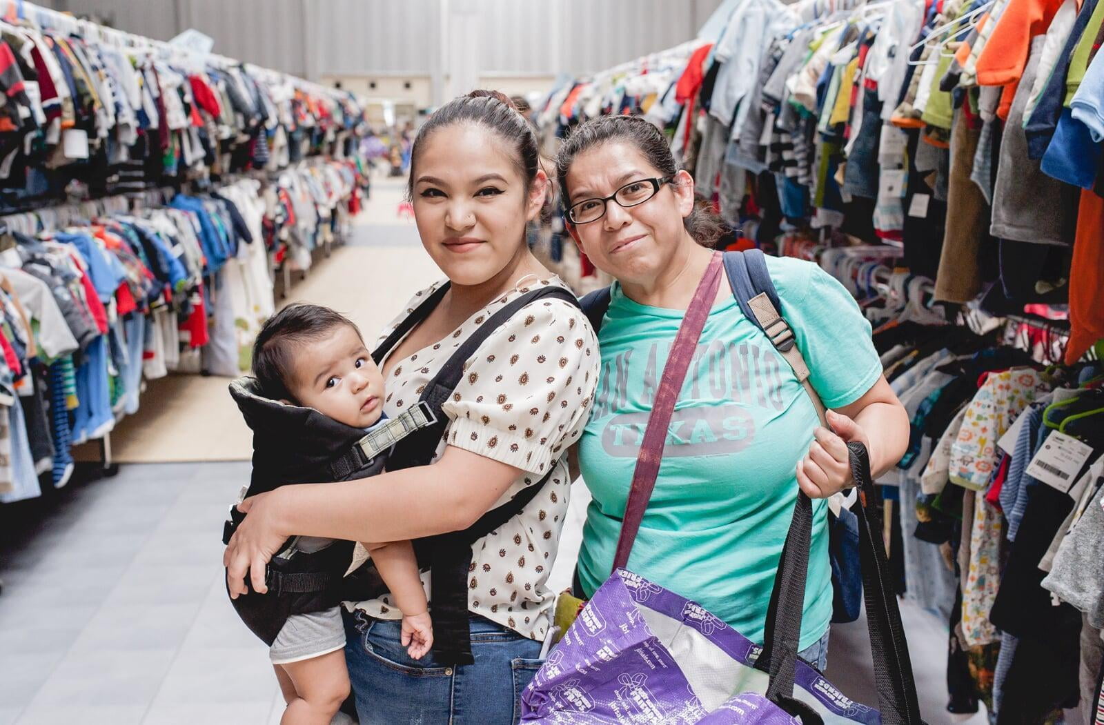 Grandmom, mom and baby in a carrier gather together and flash a smile as they shop for baby items.