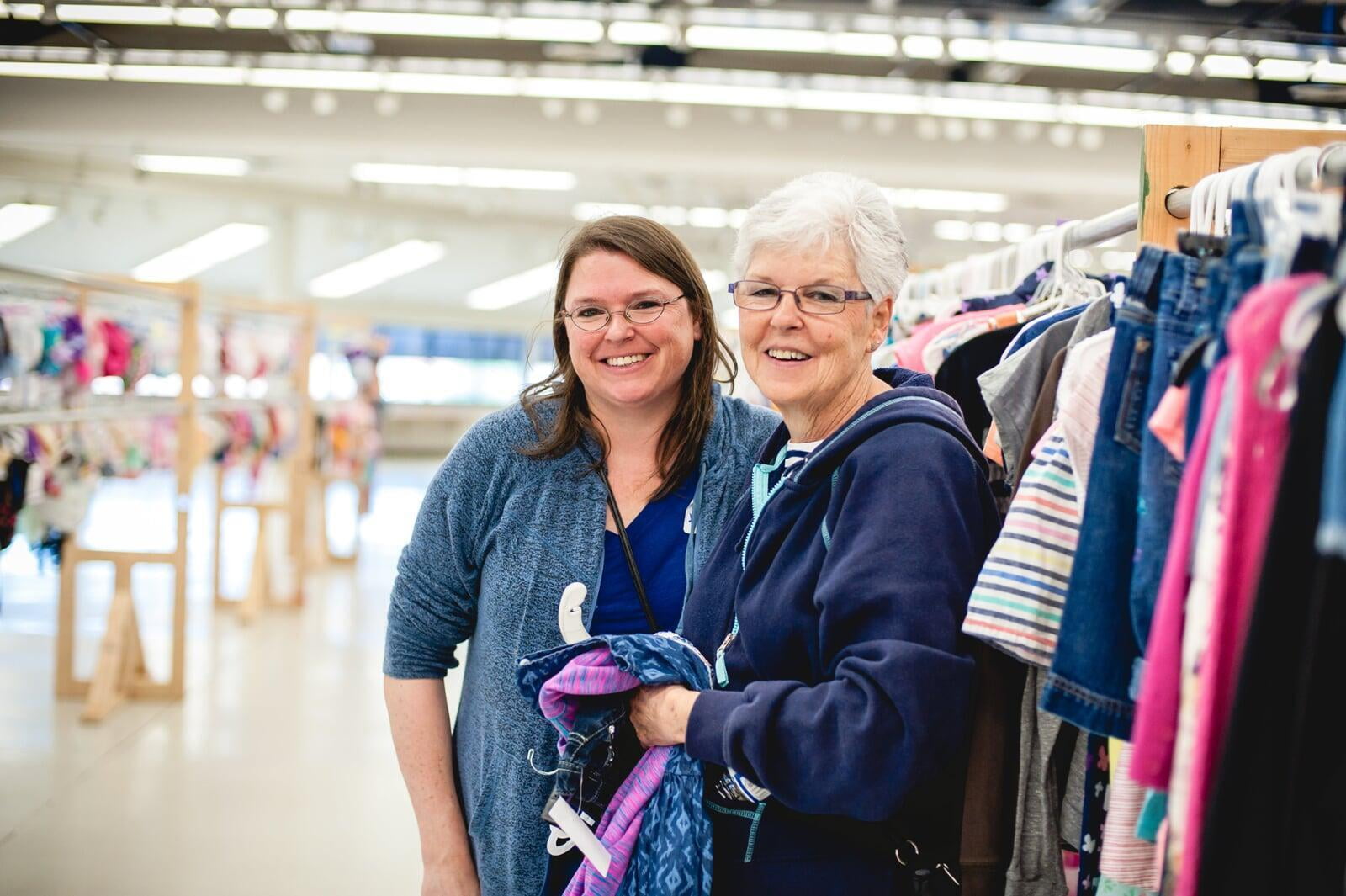 A mom and grandmother stand beside a rack of clothing at a JBF sale in Texas.